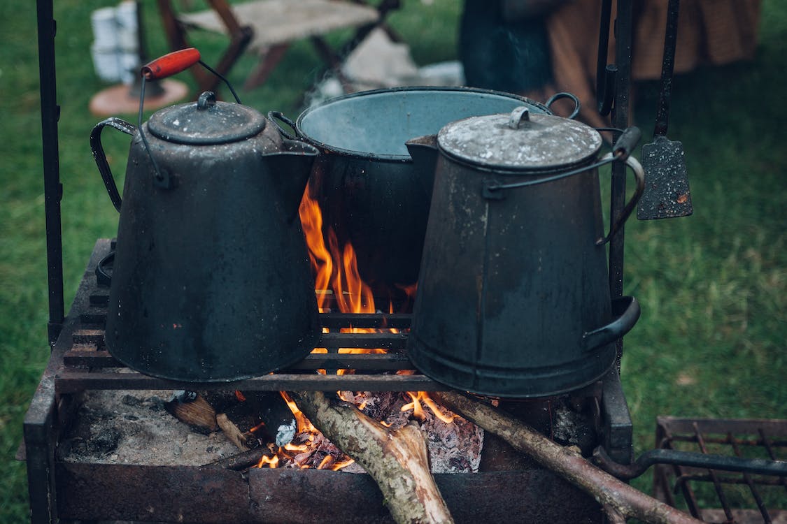 Three black and gray pots on top of the grill with fire on focus photo