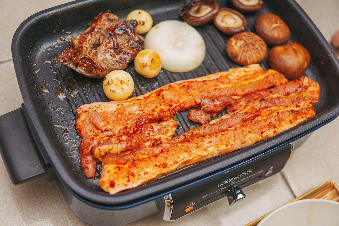 Strips of pork and piece of chicken on electric griller with onions and mushrooms