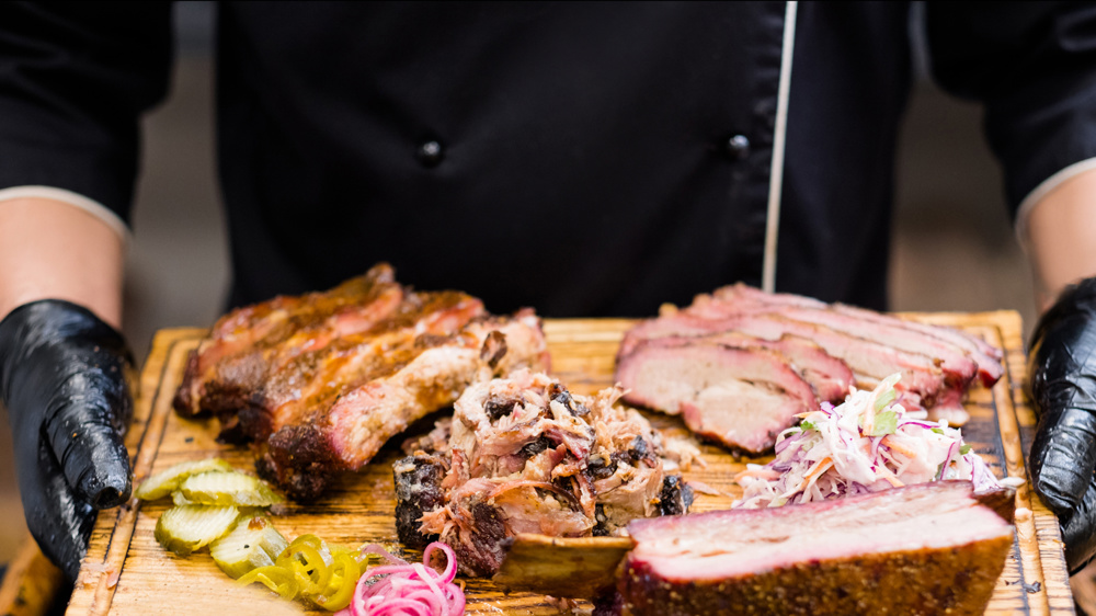 Food delivery service. Cropped shot of chef holding wooden board with smoked meat assortment, coleslaw salad, pickles
