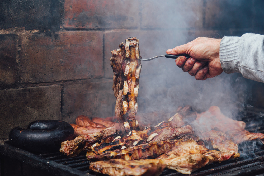 Mature man doing a bbq. He is prodding the meat with a fork. Traditional barbecue is called Asado in Argentina