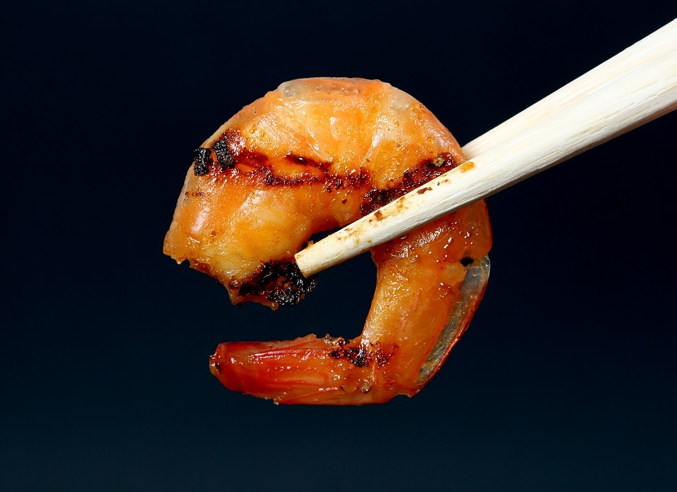 A person holding a grilled shrimp with a chopstick