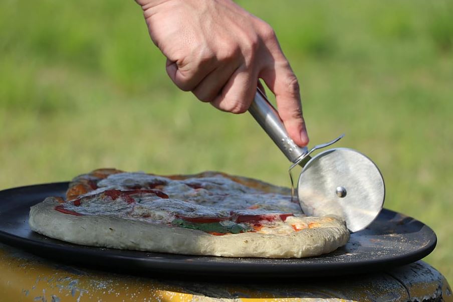 A person cutting pizza using a pizza slicer