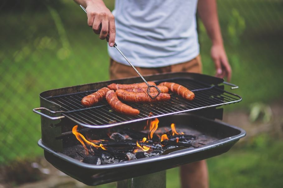A person grilling sausages on a charcoal grill