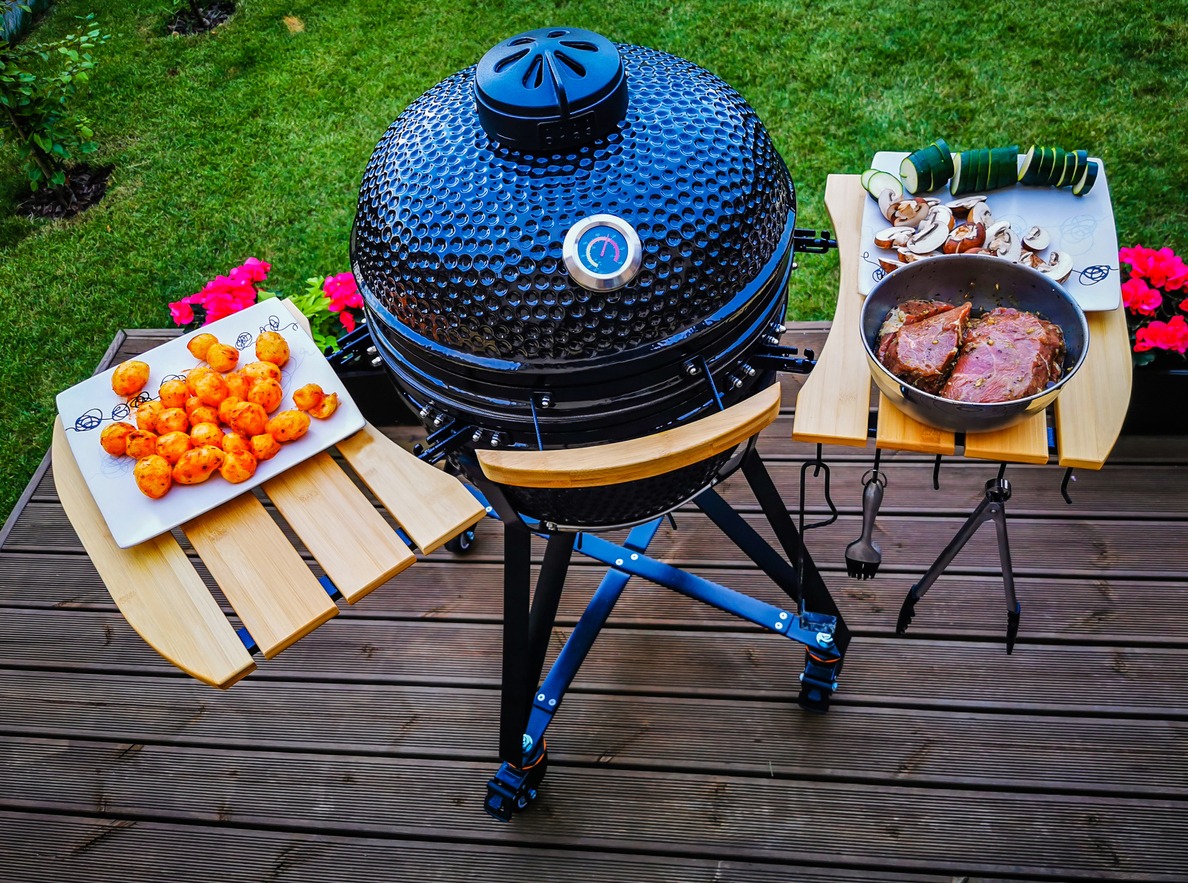 Large kamado type barbeque grill with beef steaks and vegetables ready to cook