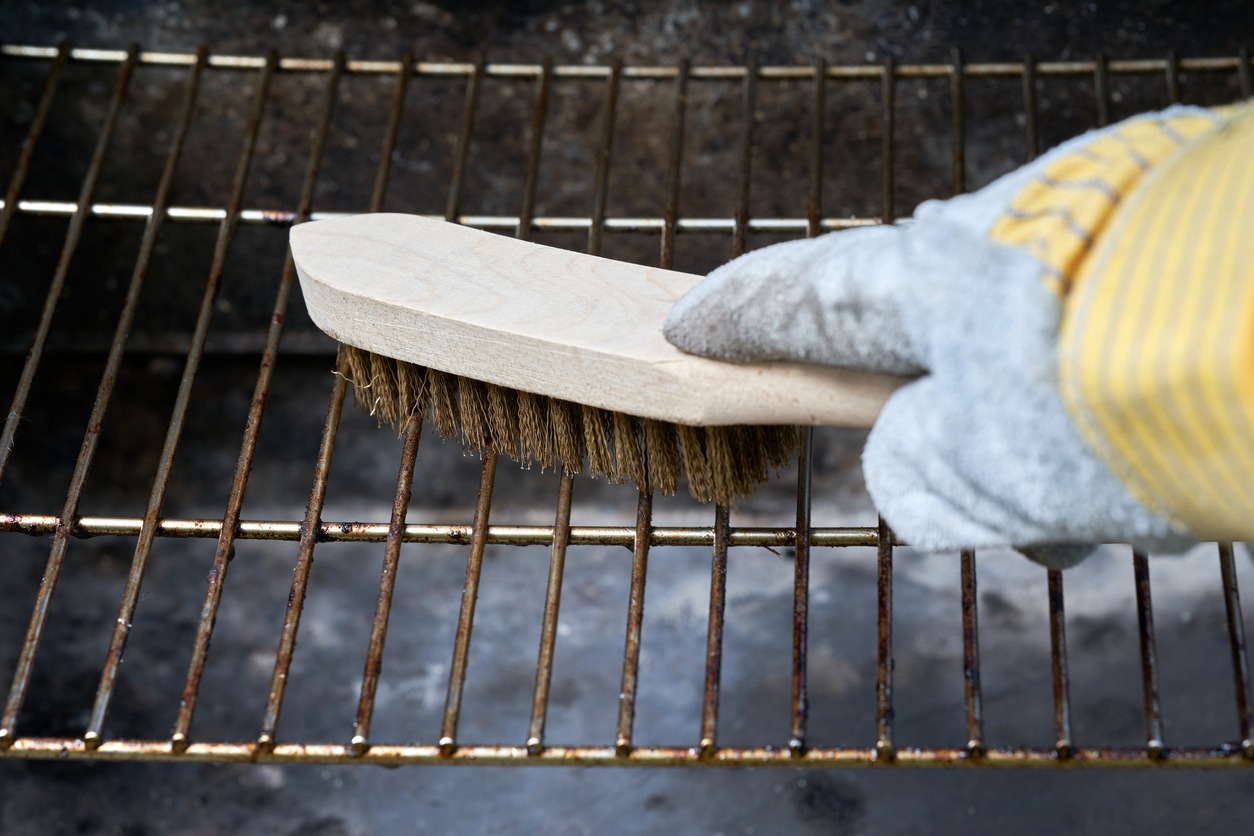 Wooden wire brush cleans dirty barbecue grill rust. Leather protection gloves.