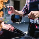 Man in Black Apron Putting Sauce on Meat while Grilling